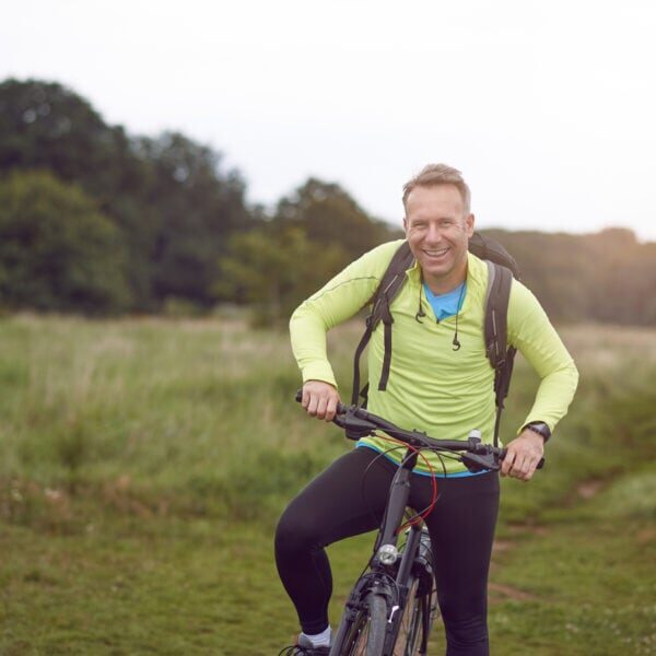 Smiling mature man wearing sportswear on bicycle tour through meadow